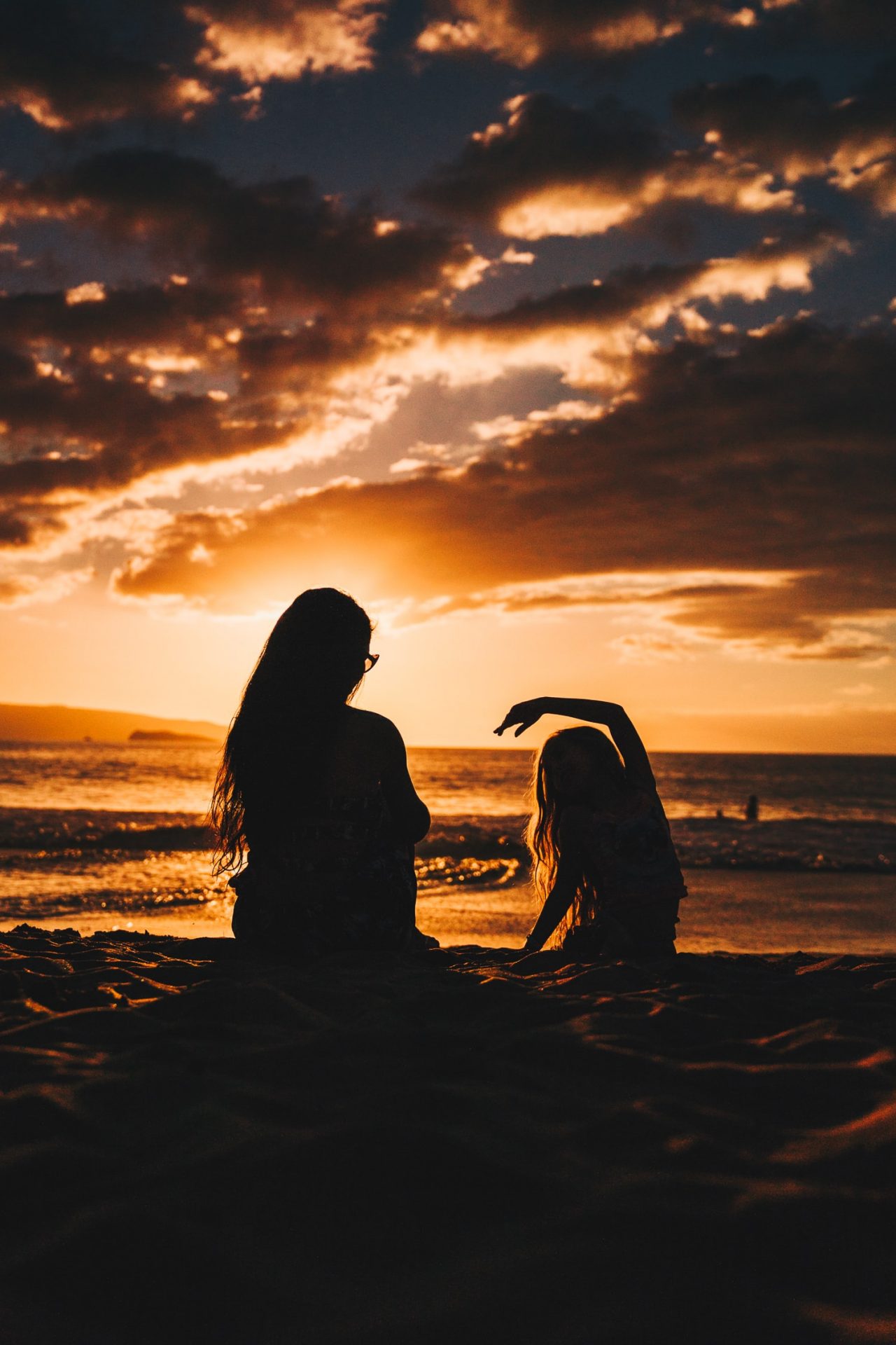 wife and daughter in front of a sunset facing the ocean
